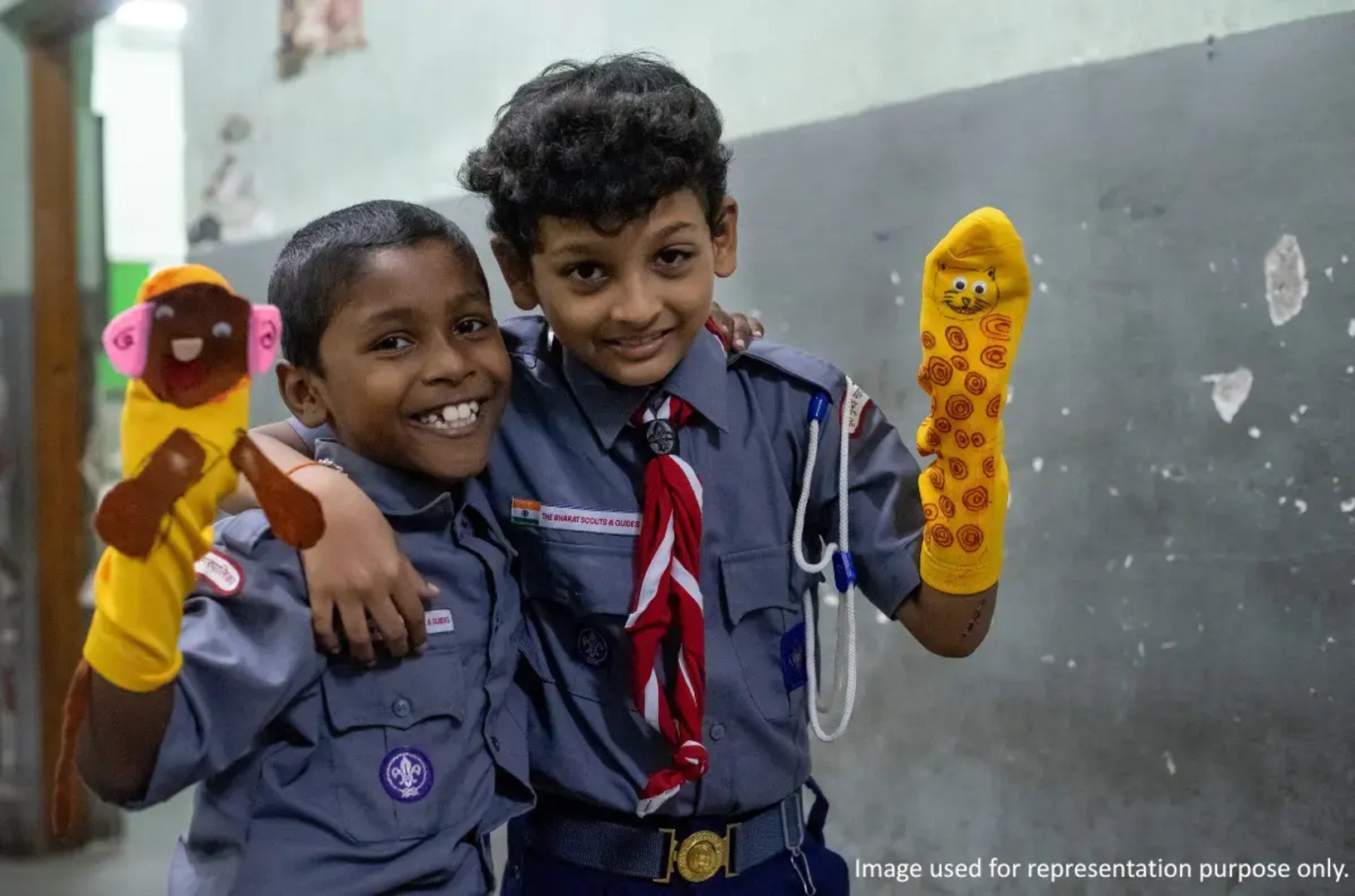Two smiling children holding hand puppets during a child development and education activity in India.