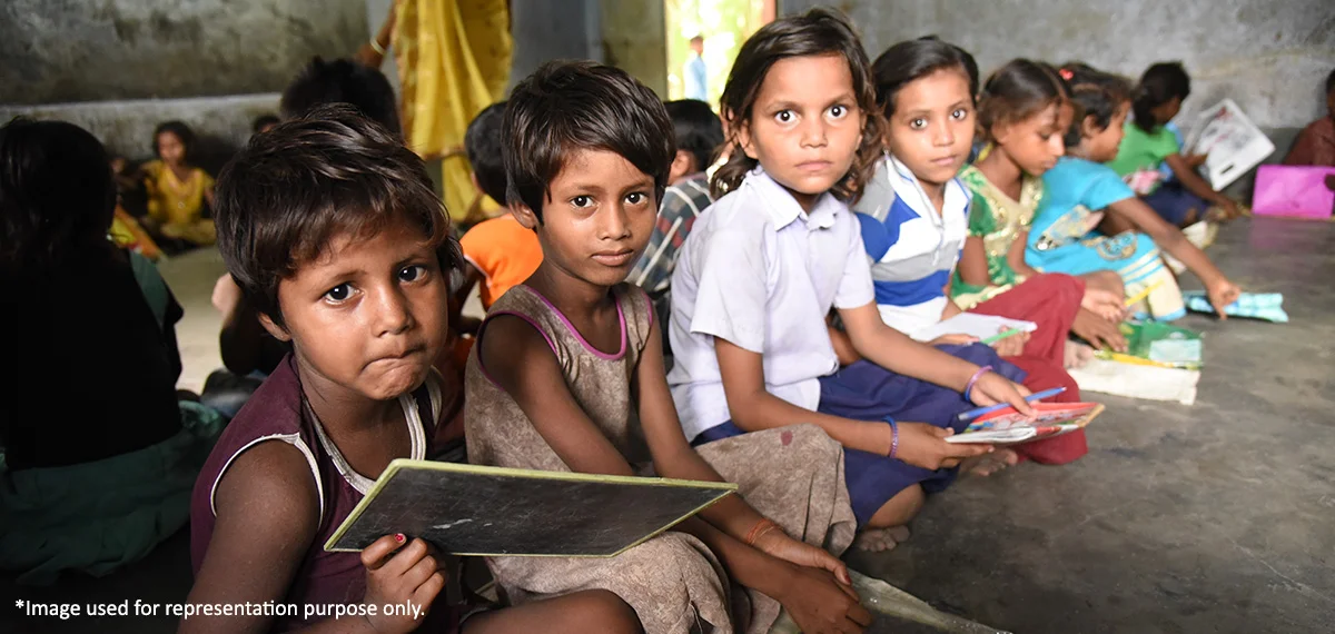Group of underprivileged children sitting in a classroom, holding books and slates, indicating the importance of education.